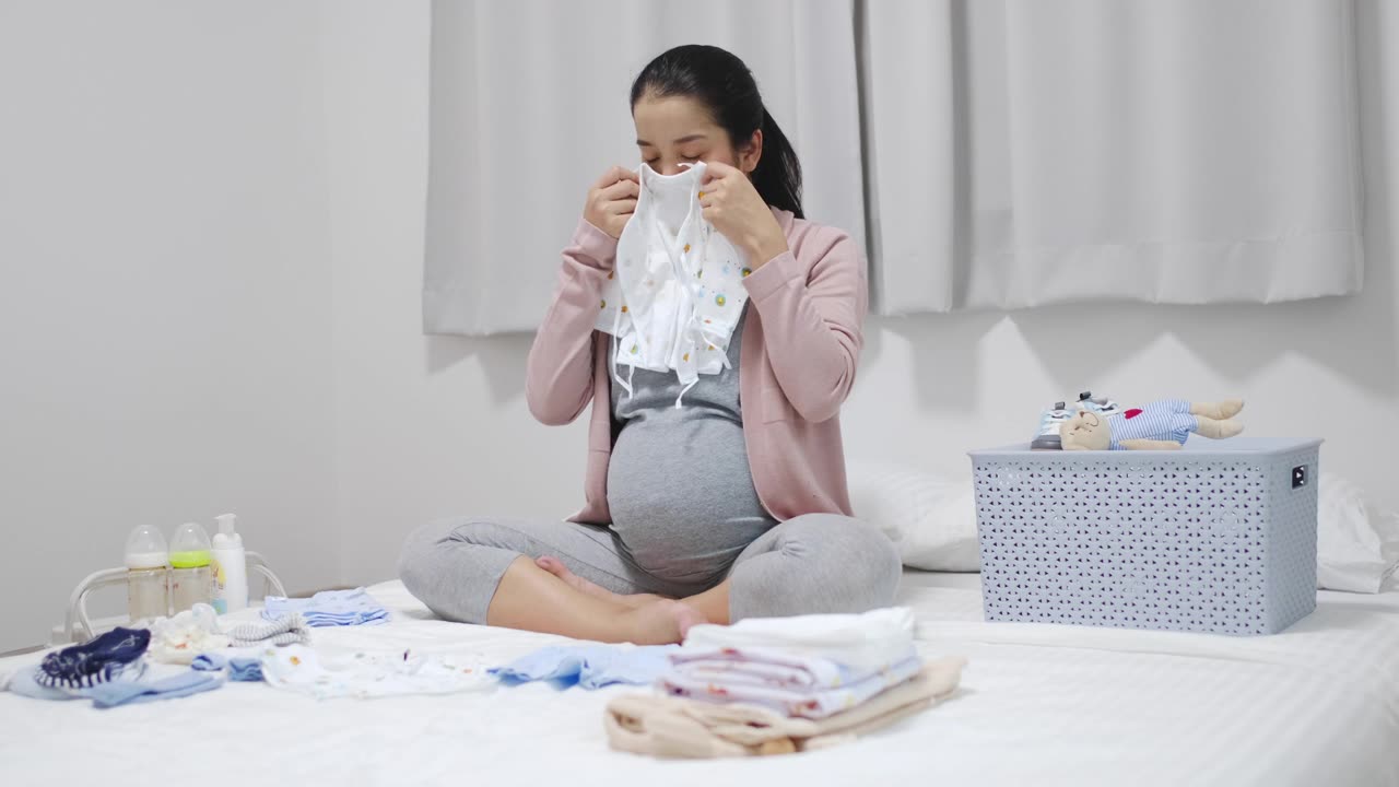 孕妇坐在卧室里，叠好婴儿的衣服，为新生儿做准备视频素材画面1