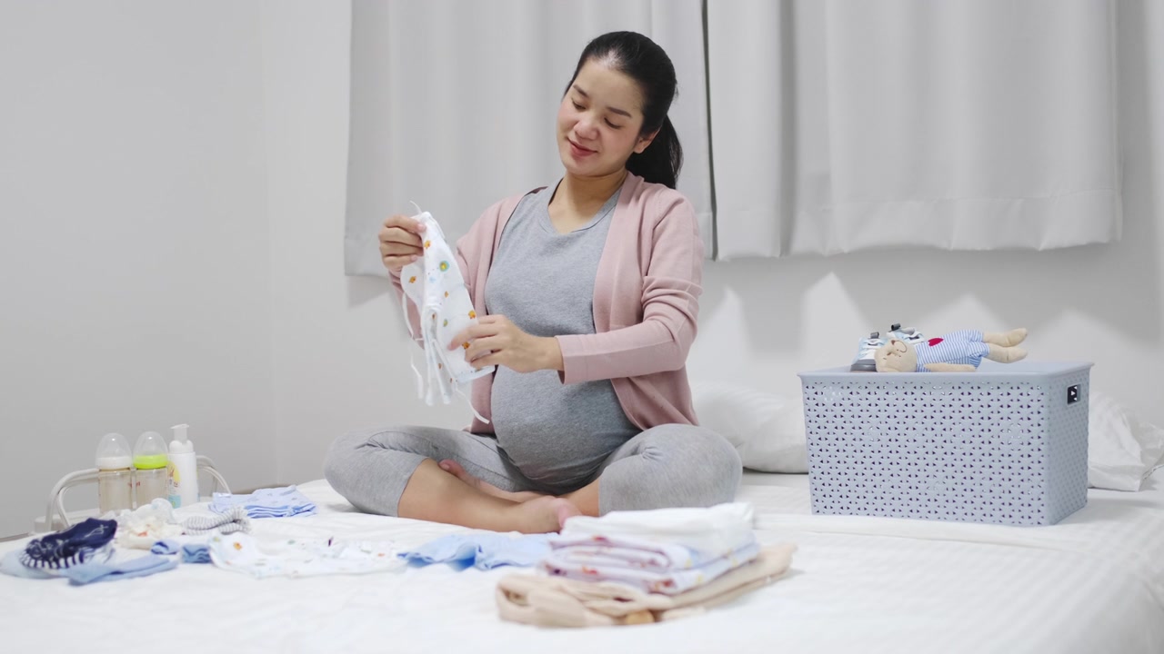 孕妇坐在卧室里，叠好婴儿的衣服，为新生儿做准备视频素材画面2