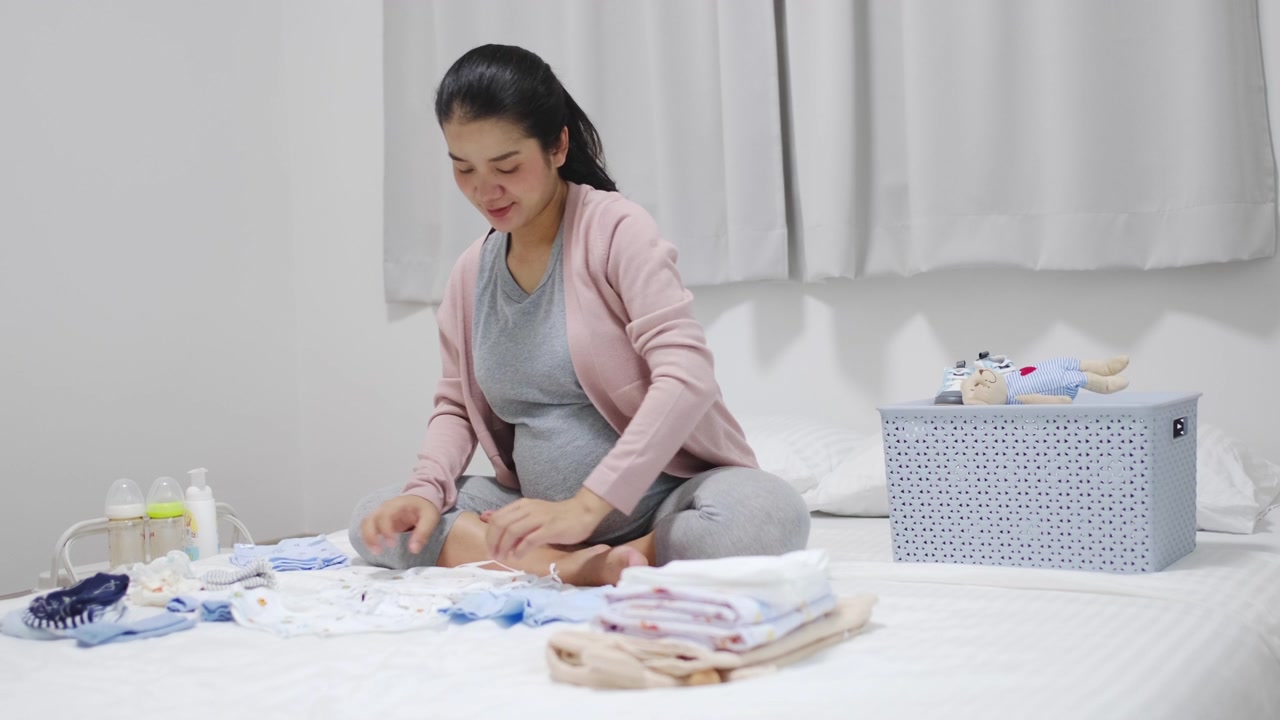 孕妇坐在卧室里，叠好婴儿的衣服，为新生儿做准备视频素材画面3
