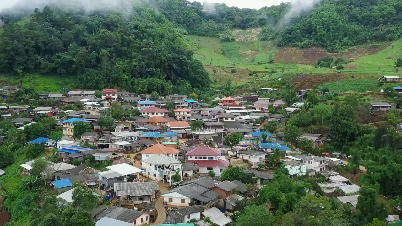 鸟瞰被群山环绕的村庄。无人机在泰国北部的乡村城市上空飞行，山和雾环绕着这个城市。视频素材