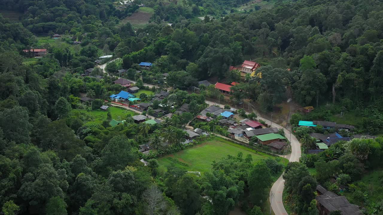 鸟瞰被群山环绕的村庄。无人机在泰国北部山区环绕的乡村城市上空飞行。视频素材