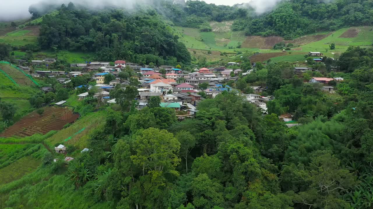 鸟瞰被群山环绕的村庄。无人机在泰国北部的乡村城市上空飞行，山和雾环绕着这个城市。视频素材