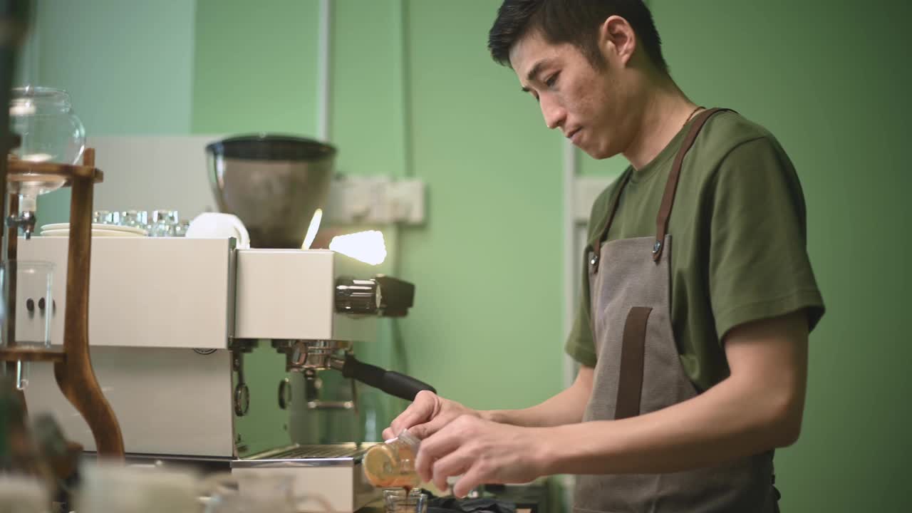 亚洲华人男咖啡师在咖啡机旁的吧台上倒浓咖啡品尝视频素材