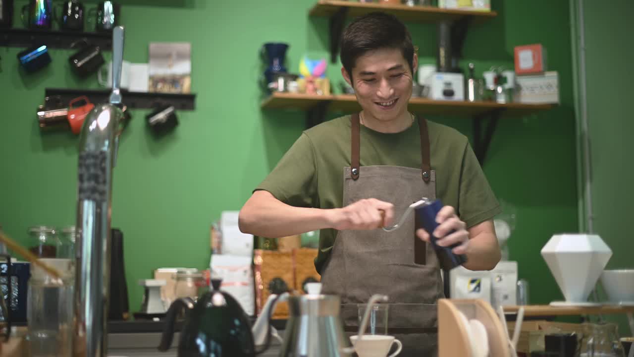 亚洲华人男咖啡师在吧台磨咖啡，为顾客准备冲泡咖啡视频素材