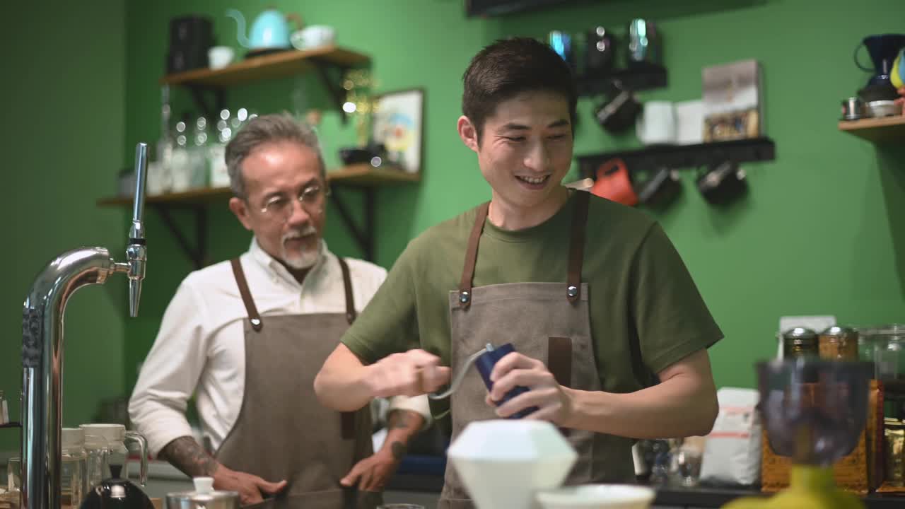 亚洲华人资深男咖啡师老板喜欢和在吧台磨咖啡的员工聊天视频素材