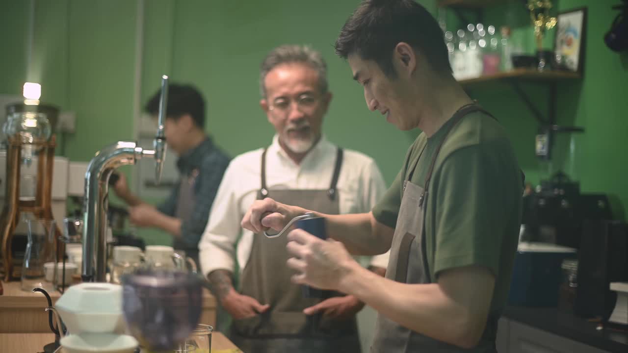 亚洲华人资深男咖啡师老板喜欢和在吧台磨咖啡的员工聊天视频素材