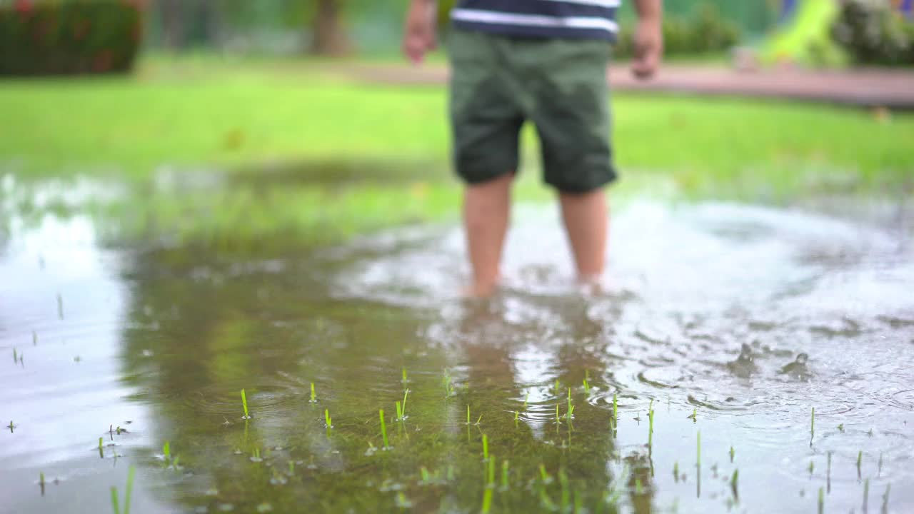 蹒跚学步的男孩在公园的水坑上跳跃视频素材