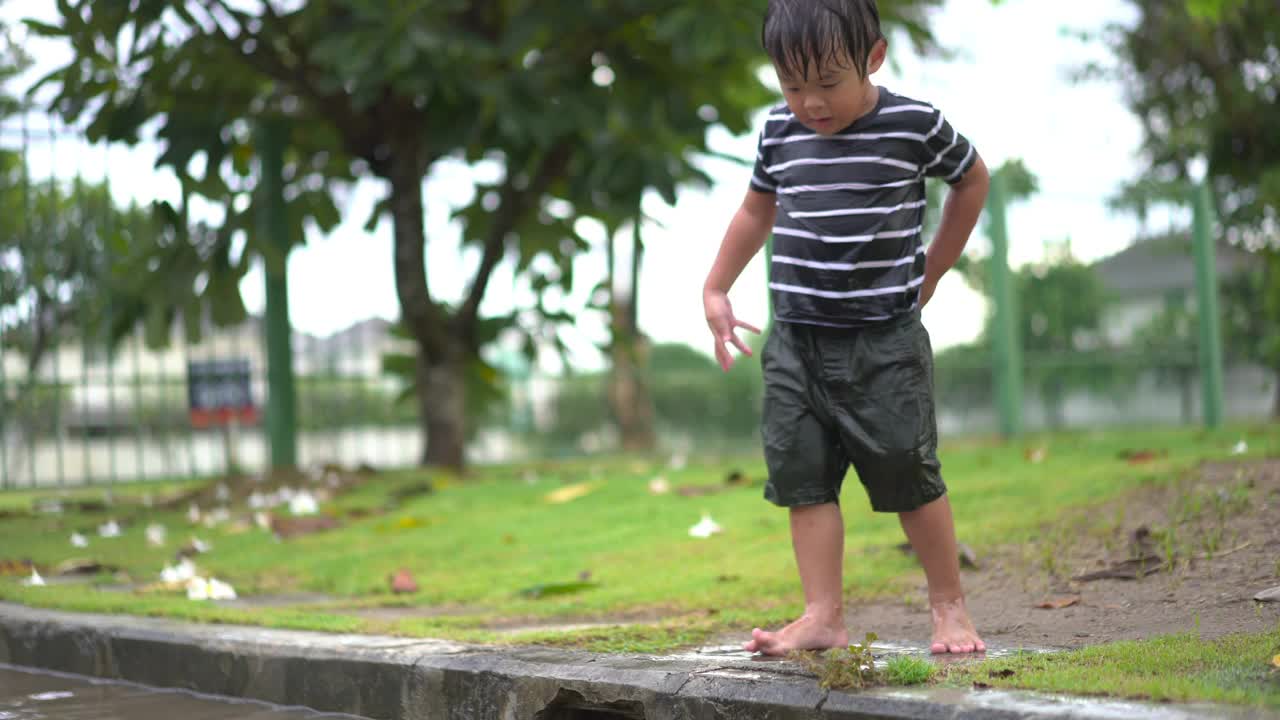 蹒跚学步的小男孩在村庄路上的水坑上跳来跳去视频素材