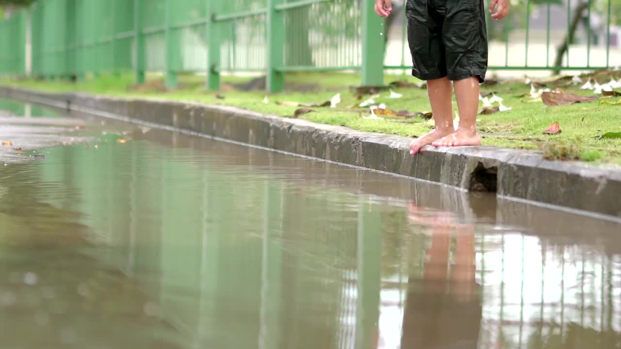 慢动作蹒跚学步的男孩在村里的路上的水坑上跳视频素材