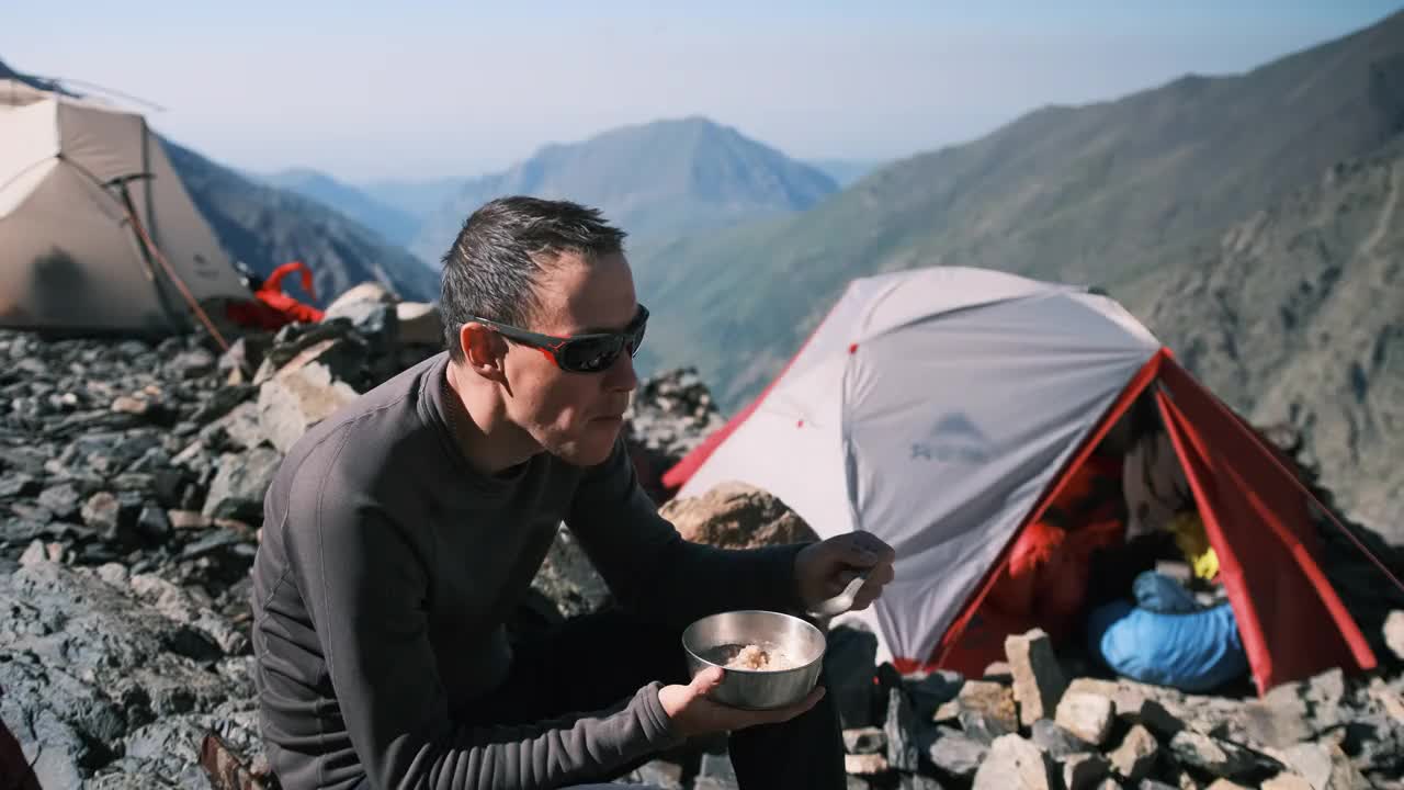 登山运动员在徒步旅行时坐在岩石上吃早餐。视频素材