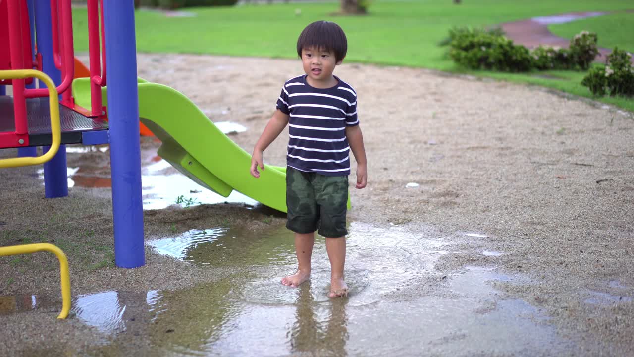 操场上，雨后坐在水坑里的可爱男孩视频素材