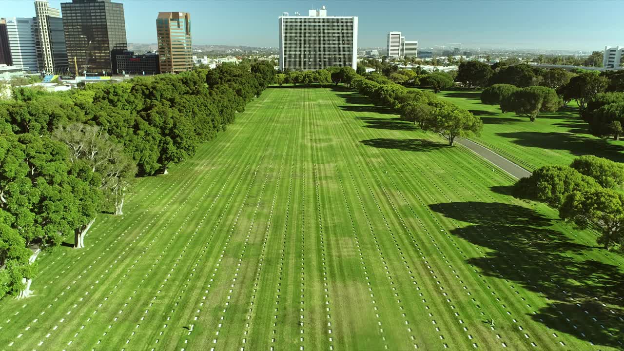 WS跟踪穿过国家公墓广阔的墓地，数千个白色的军事墓碑对称地排列在绿色草坪上，也显示在威斯特伍德Wilshire大道的摩天大楼的背景视频素材