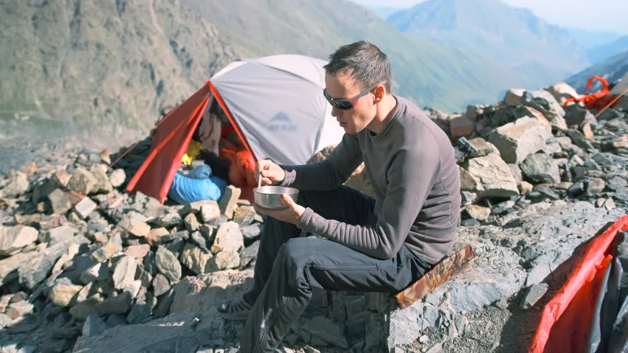 在山区的登山营里，一名手里拿着盘子的游客正在吃早餐。视频素材