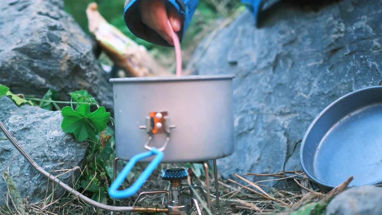 在一次野营中，一个妇女的手在炉子上的锅里搅拌沸水准备食物视频素材