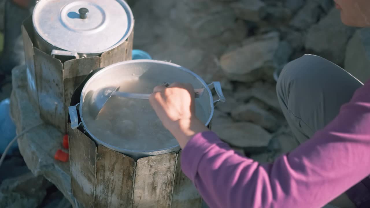 徒步旅行时，一位妇女正在用长柄勺搅拌煮好的粥。视频素材