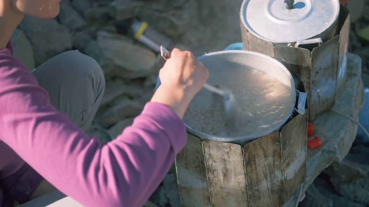 徒步旅行时，一个女孩在大炖锅里用勺子搅拌煮好的粥视频素材