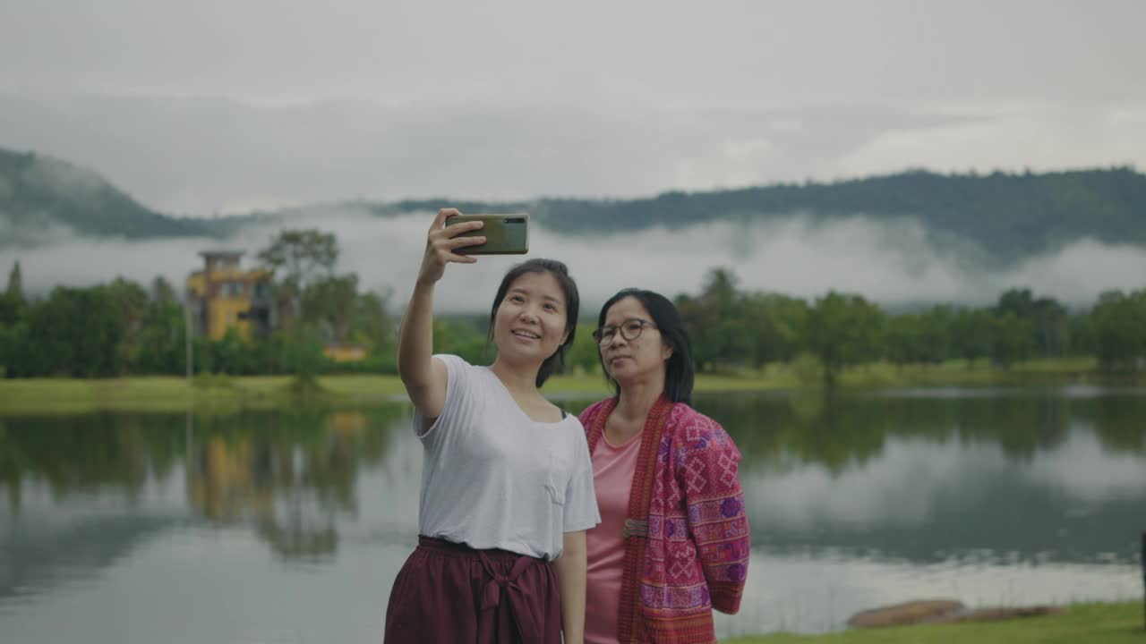 母女俩一边自拍一边欣赏着湖边和雨林山的美景。视频素材