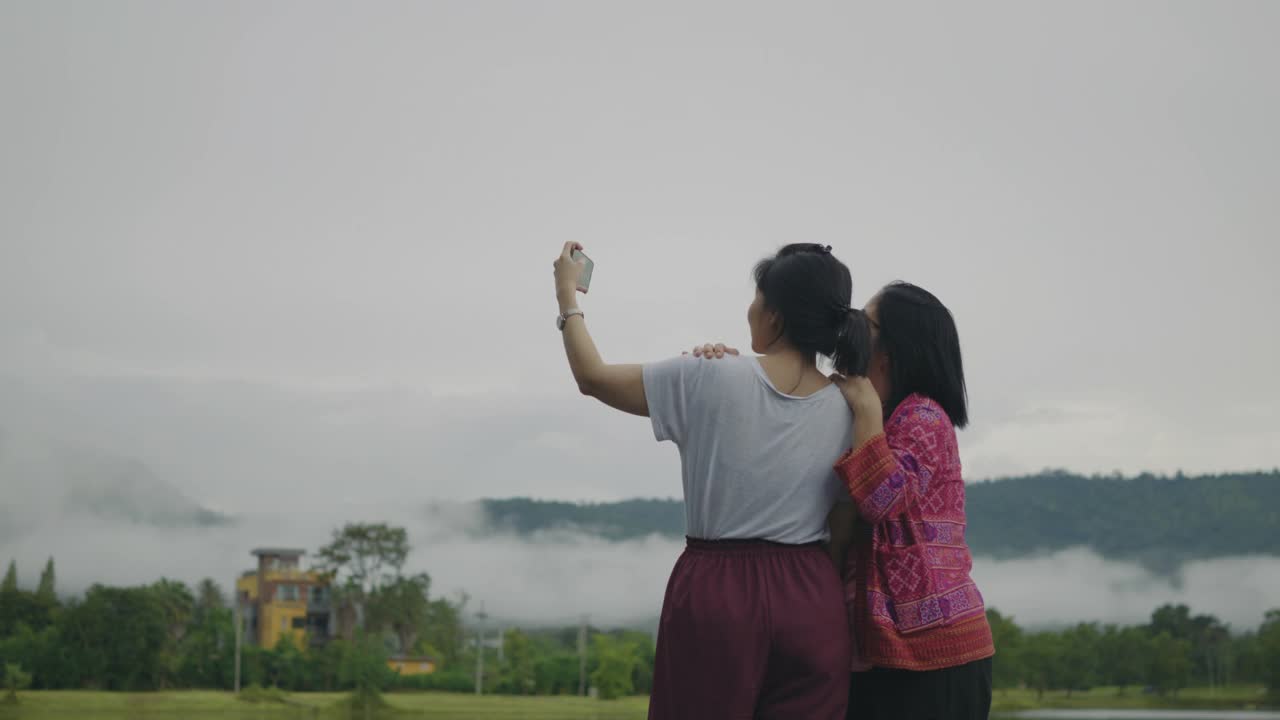 母女俩一边自拍一边欣赏着湖边和雨林山的美景。视频下载