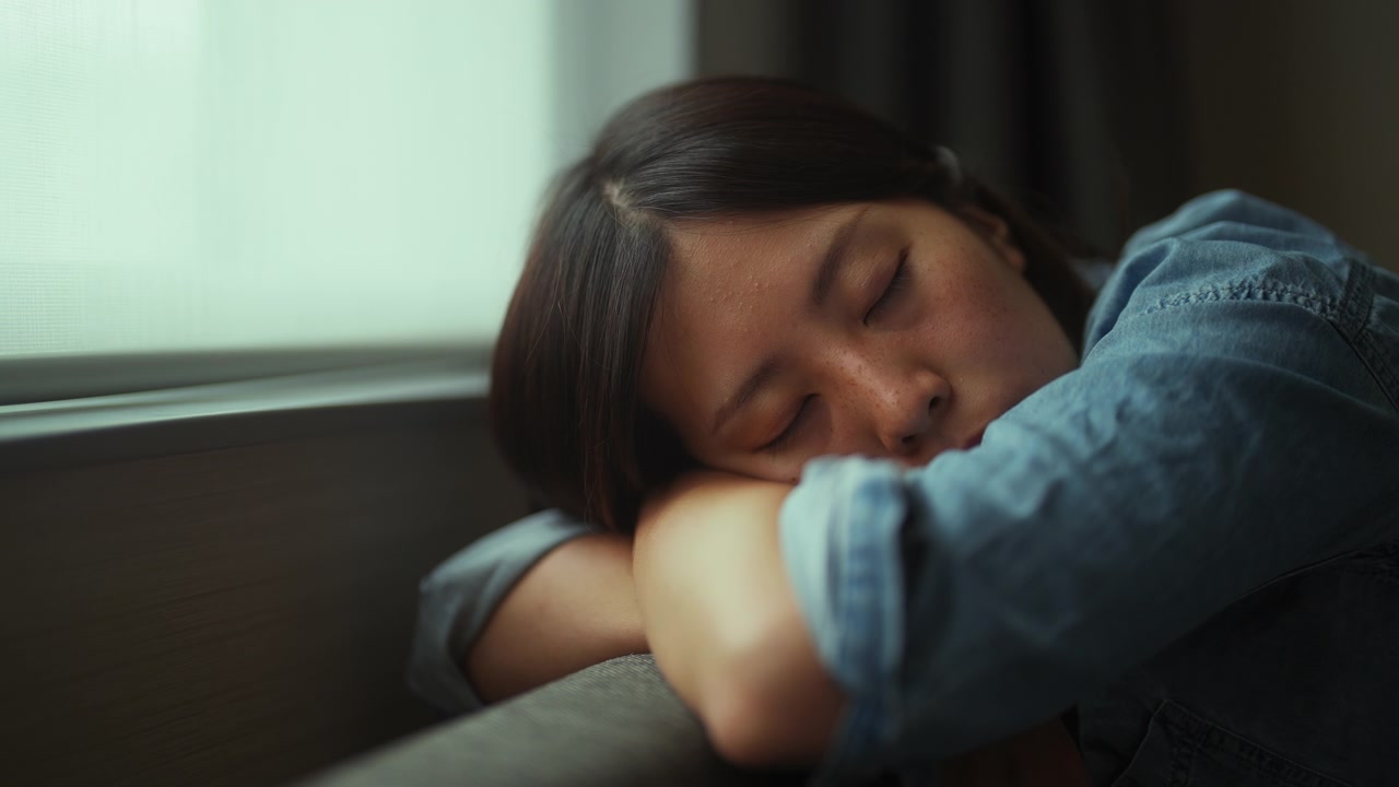 年轻女子坐在沙发上，睡在家里的窗边视频素材画面2
