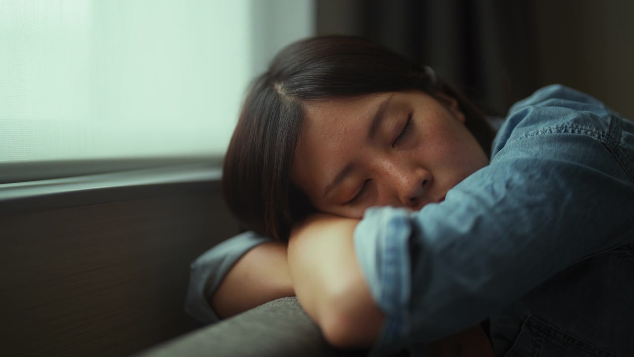 年轻女子坐在沙发上，睡在家里的窗边视频素材画面3