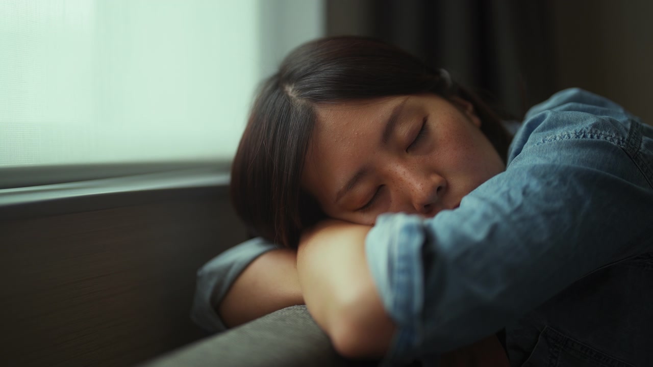 年轻女子坐在沙发上，睡在家里的窗边视频素材画面4