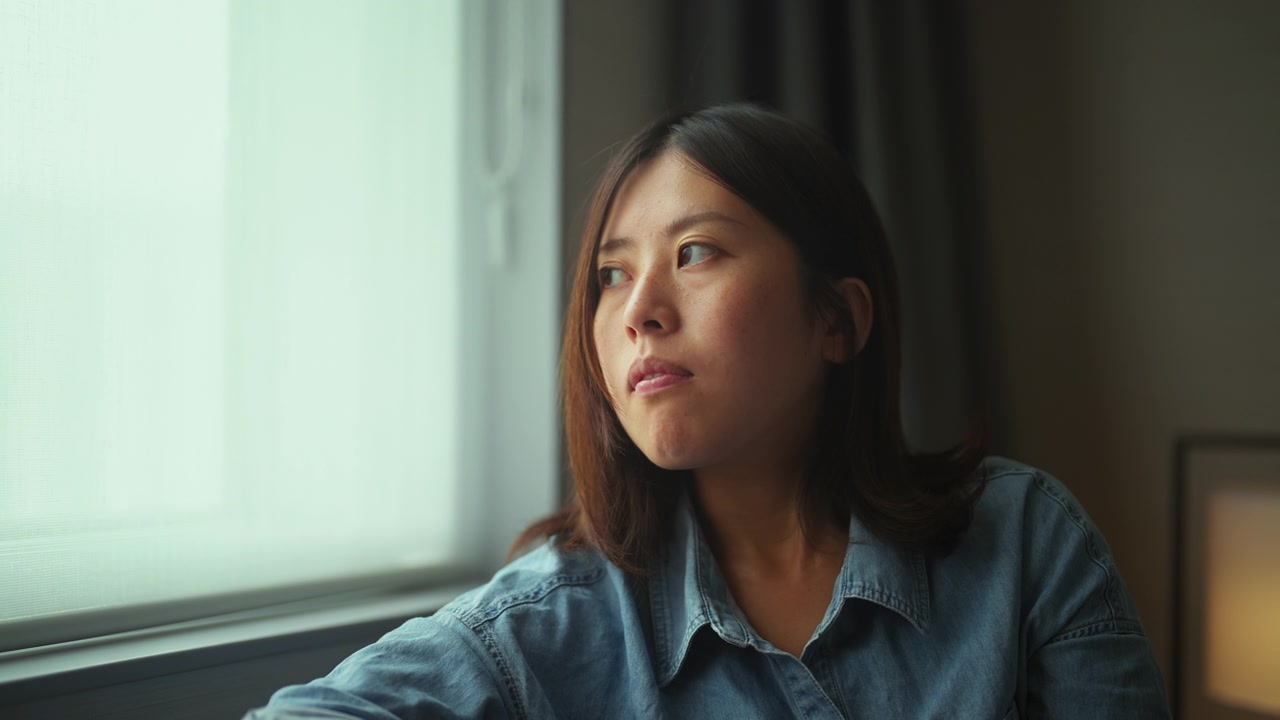 年轻女子坐在靠窗的沙发上，用着智能手机回家视频素材画面2