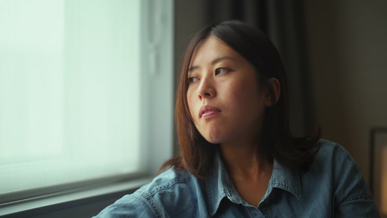 年轻女子坐在靠窗的沙发上，用着智能手机回家视频素材画面3