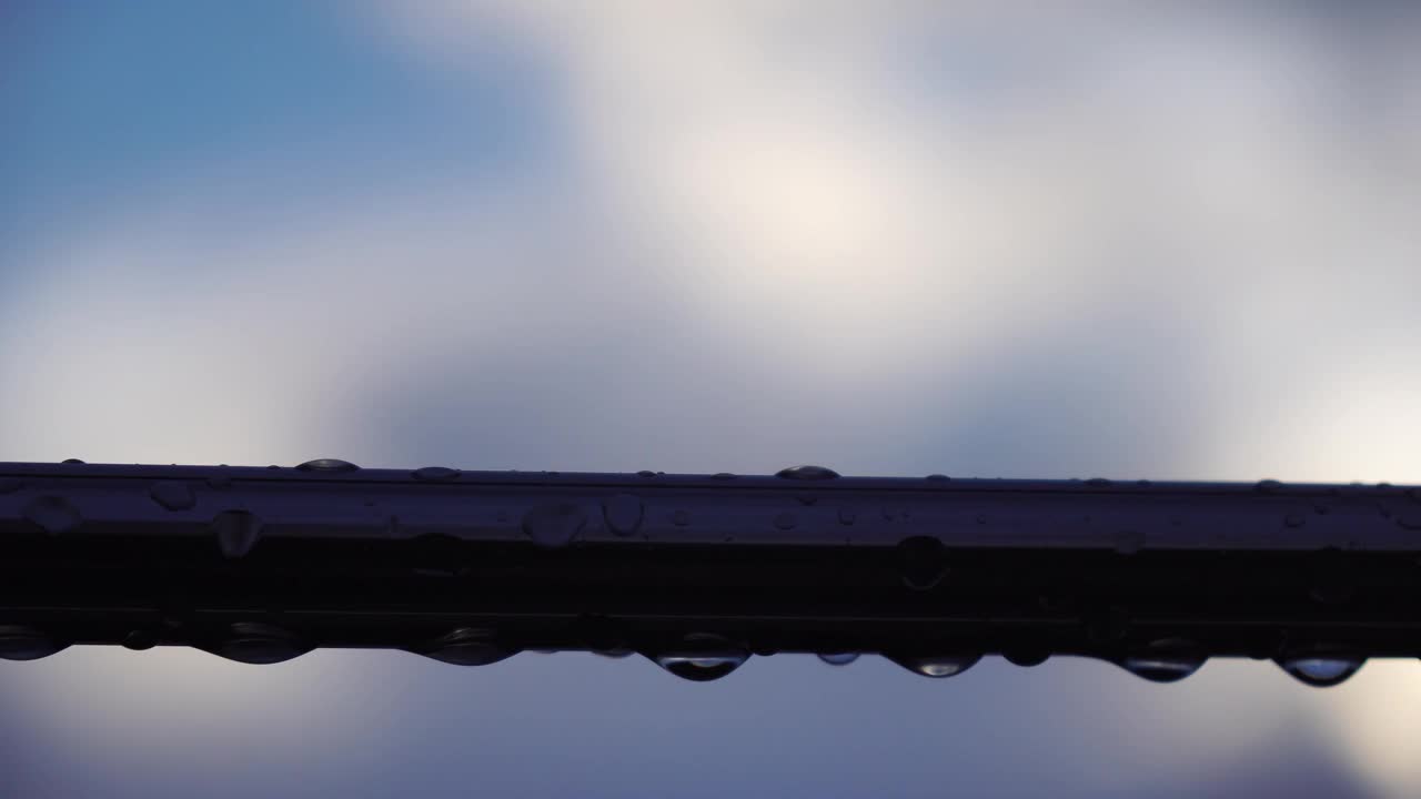 不锈钢扶手上的雨滴映衬着模糊的大海背景。特写镜头。雨露的水滴聚集在闪闪发光的铬钢杆扶手上视频素材