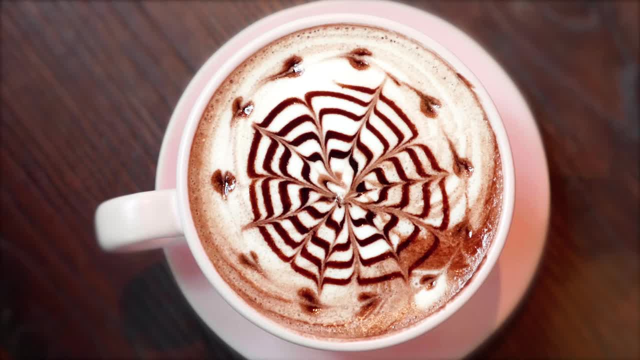 Top View of Pink Cup of Coffee with Latte Art from Chocolate Syrup in Cafe .粉红杯拿铁咖啡来自巧克力糖浆视频素材