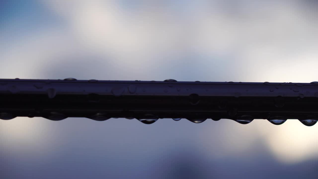 不锈钢扶手上的雨滴映衬着模糊的大海背景。特写镜头。雨露的水滴聚集在闪闪发光的铬钢杆扶手上视频素材