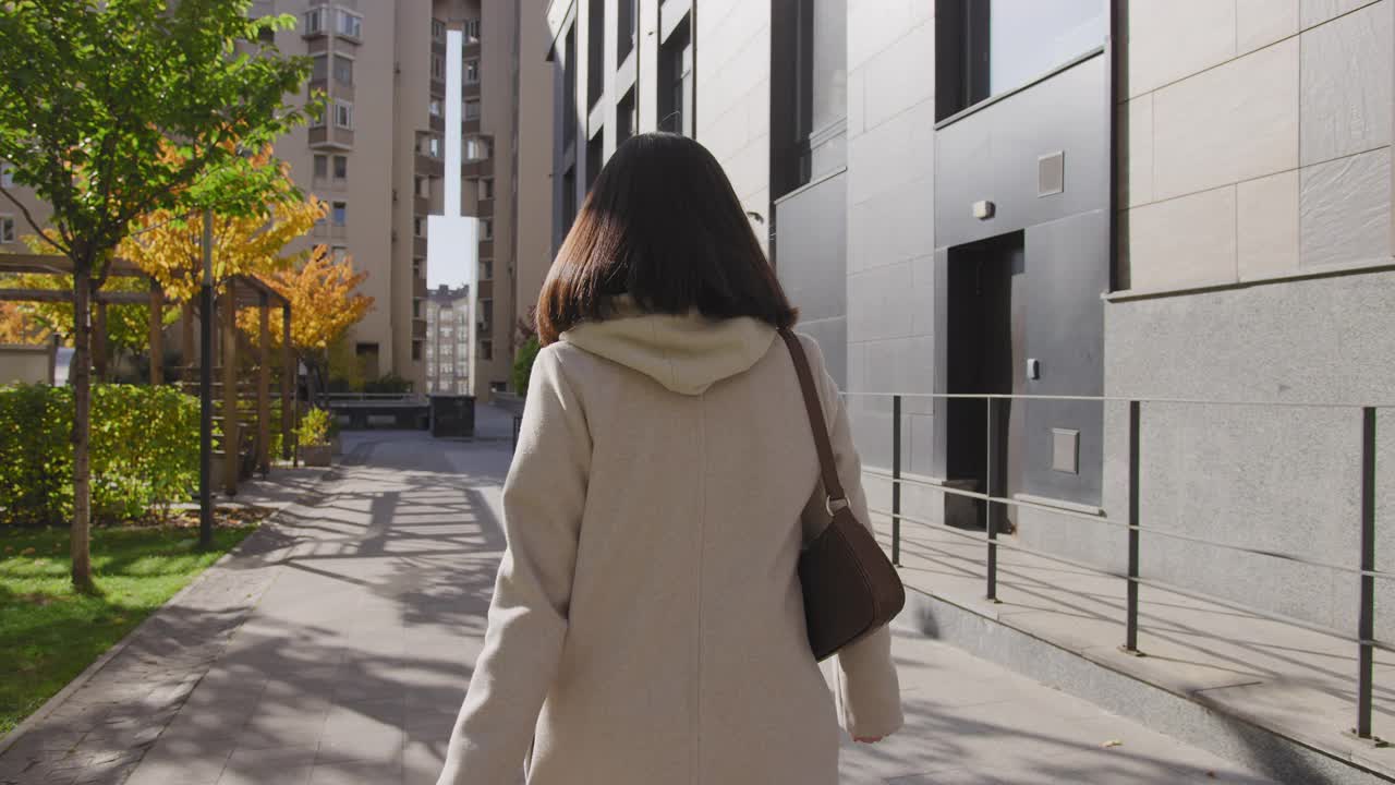 一位年轻的成年妇女走在城市街道的金色树木之间视频素材