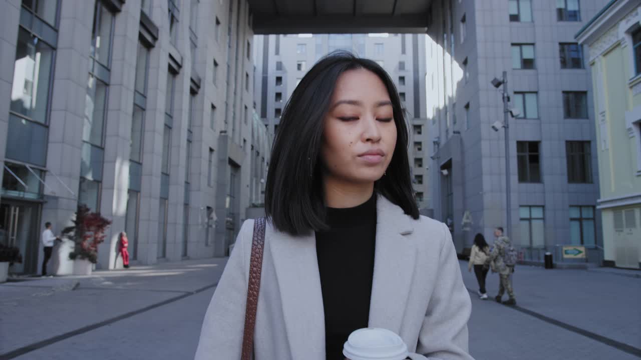 年轻的亚洲女商人从办公室走出来，手里拿着一个咖啡杯视频素材