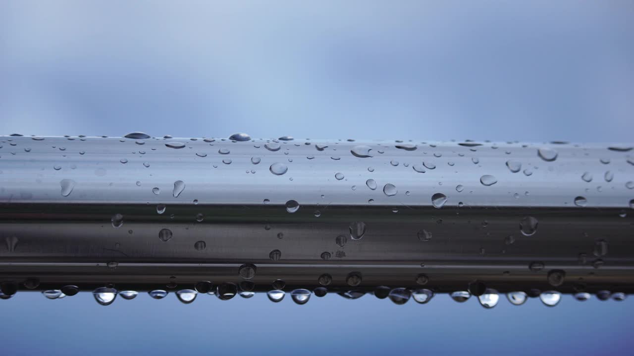 不锈钢扶手上的雨滴映衬着模糊的大海背景。特写镜头。雨露的水滴聚集在闪闪发光的铬钢杆扶手上视频素材