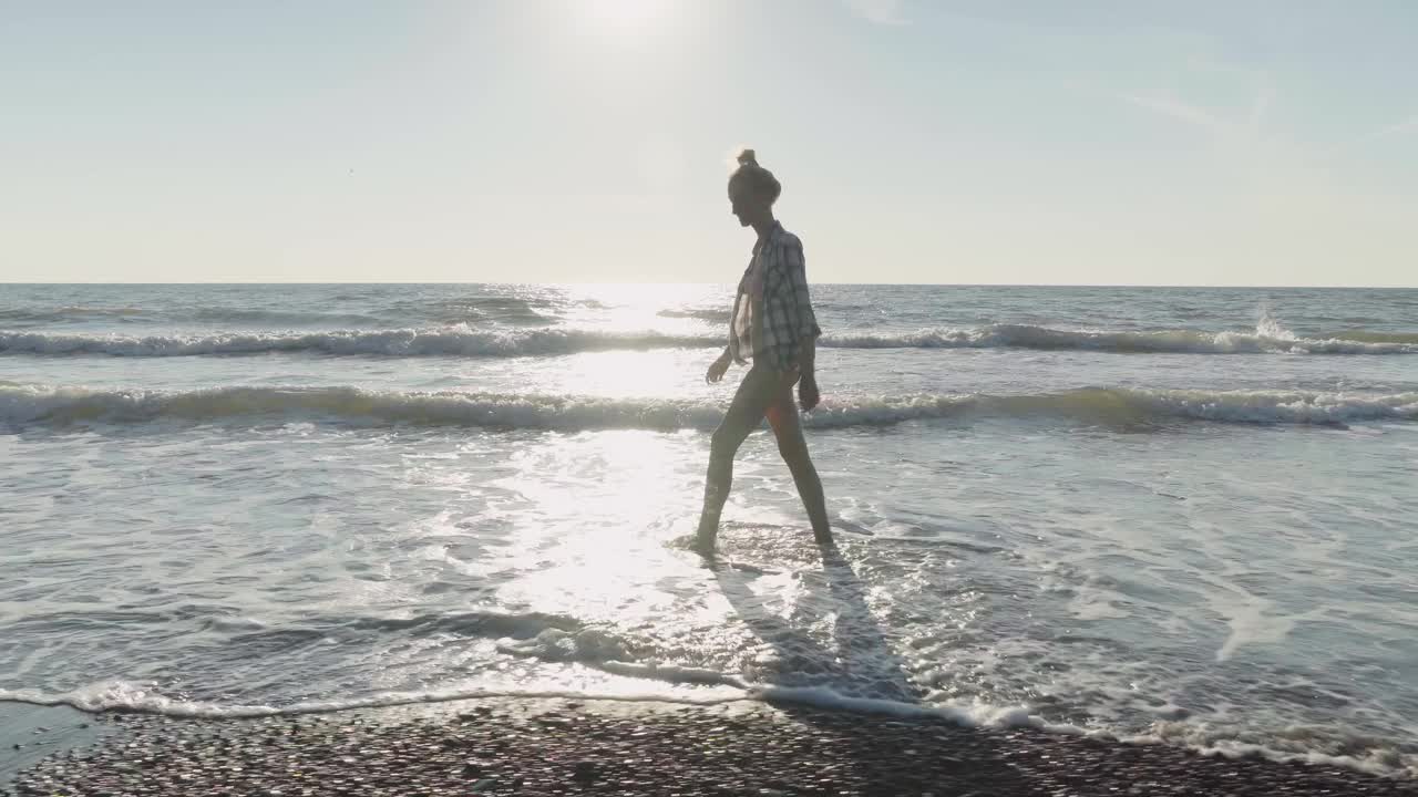 一个苗条的女人走在沙滩上的海浪上。视频素材