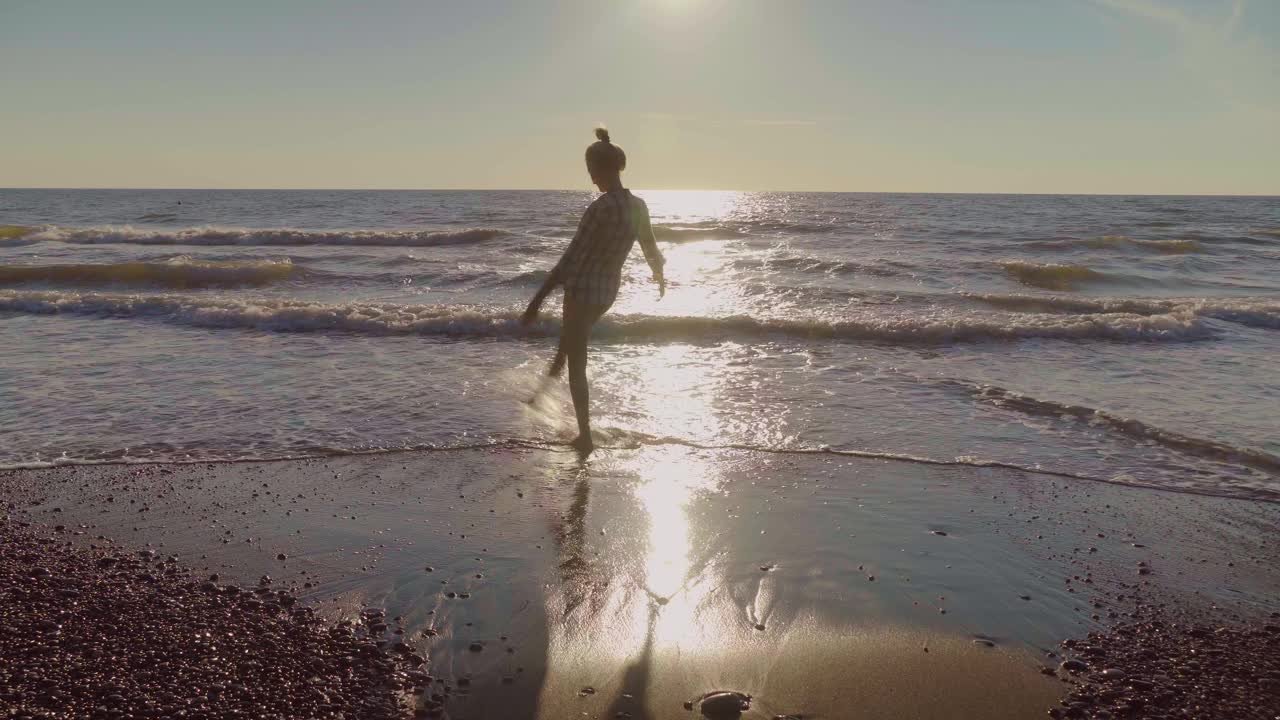 苗条的女人在沙滩上踢海水。飞溅的水视频素材