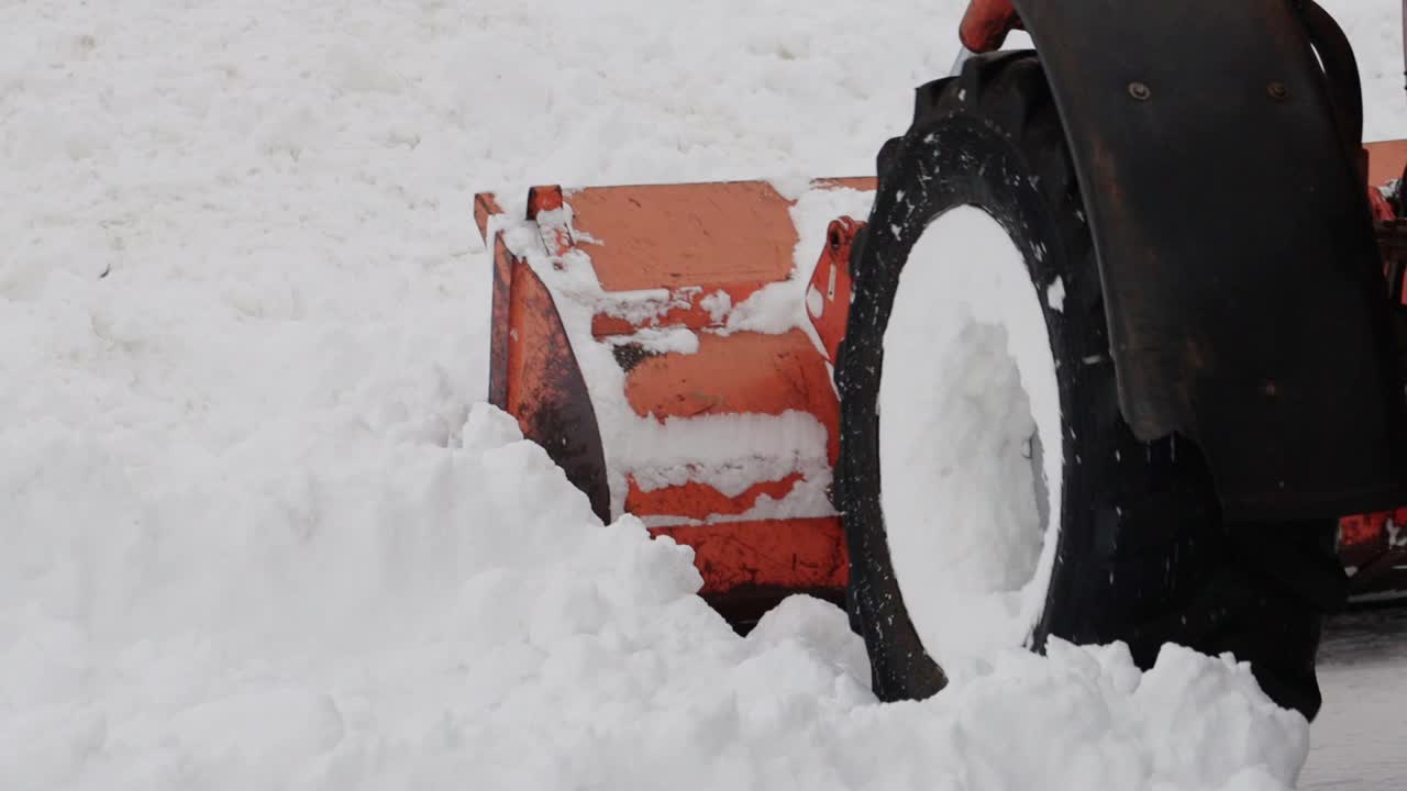 冬天，一辆带着黄色铲斗的拖拉机在街上铲雪。道路清扫援助。慢动作视频素材