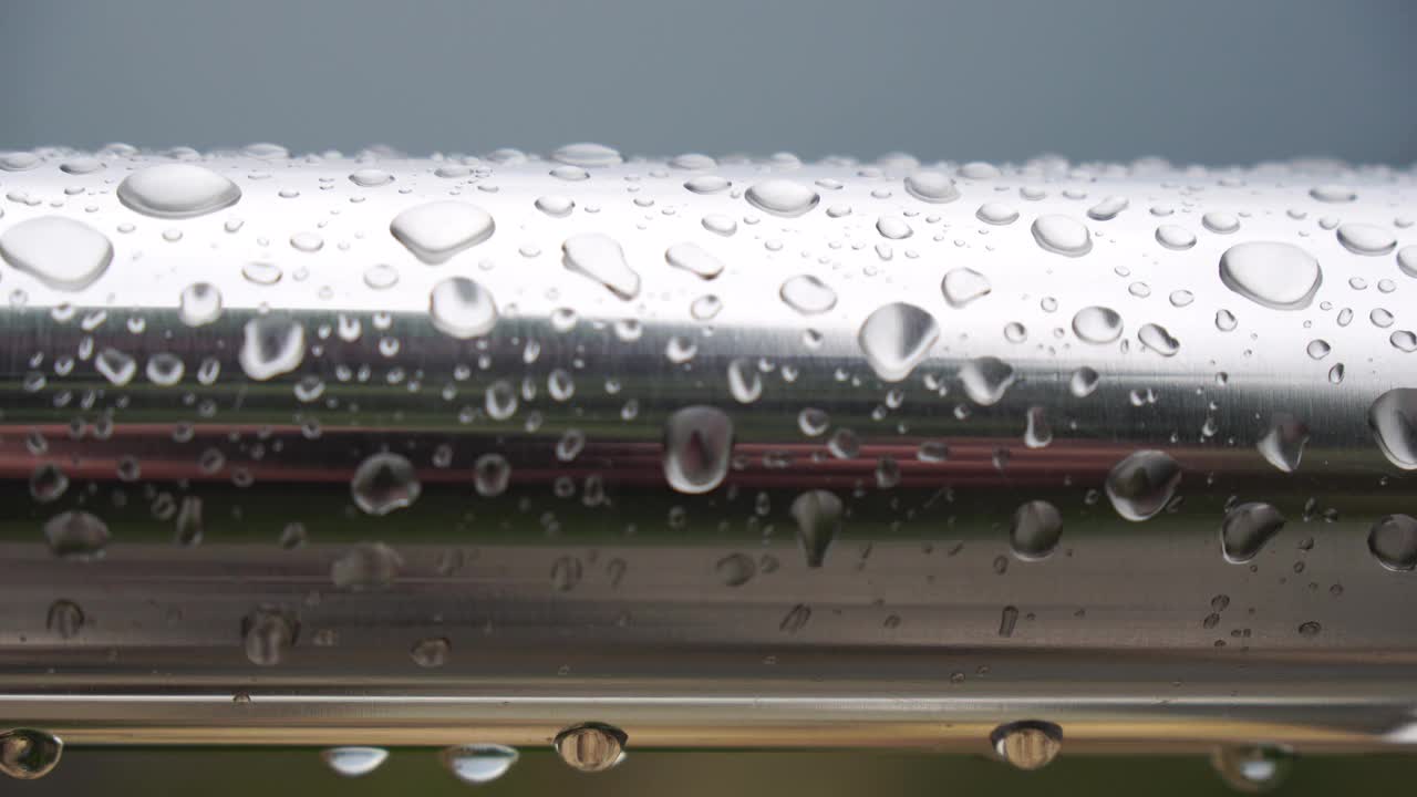 不锈钢扶手上的雨滴映衬着模糊的大海背景。特写镜头。雨露的水滴聚集在闪闪发光的铬钢杆扶手上视频素材