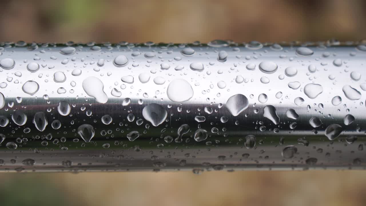 不锈钢扶手上的雨滴映衬着模糊的大海背景。特写镜头。雨露的水滴聚集在闪闪发光的铬钢杆扶手上视频素材