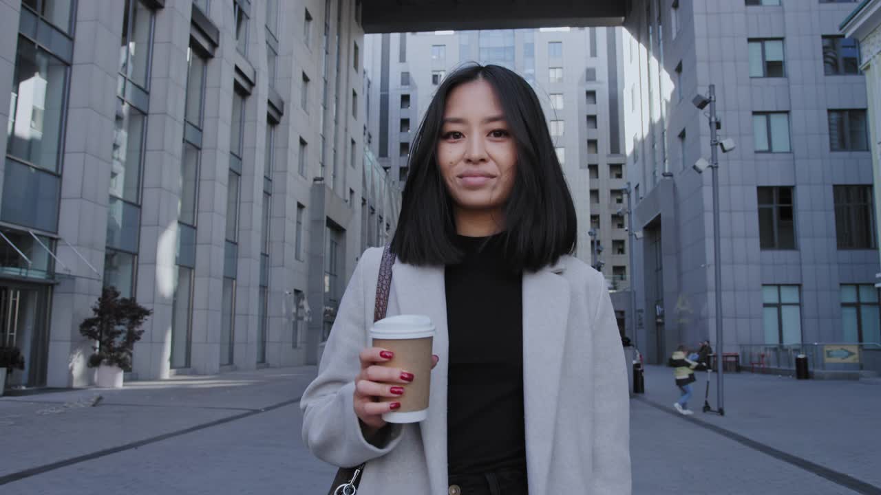 年轻的亚洲女商人从办公室走出来，拿着一个咖啡杯，慢动作视频素材