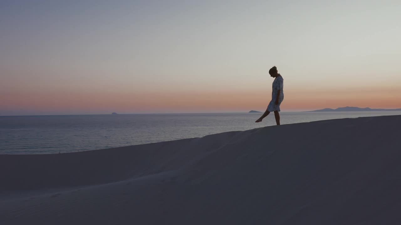 意大利撒丁岛，一个女人坐在日落时的海滩上。视频素材