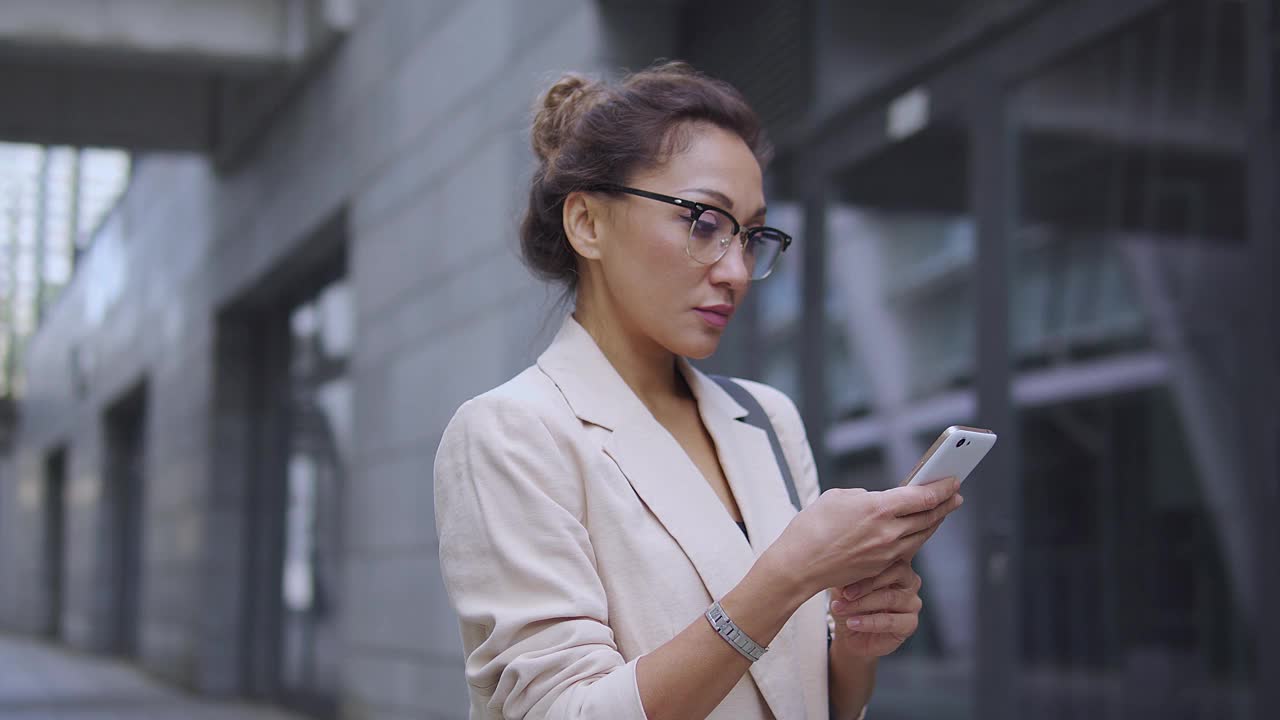 自信美丽的女性危机经理，穿着优雅的西装，戴着眼镜，检查公司费率，分析情况，寻求问题的解决方案，运营研究分析师在智能手机上工作视频素材