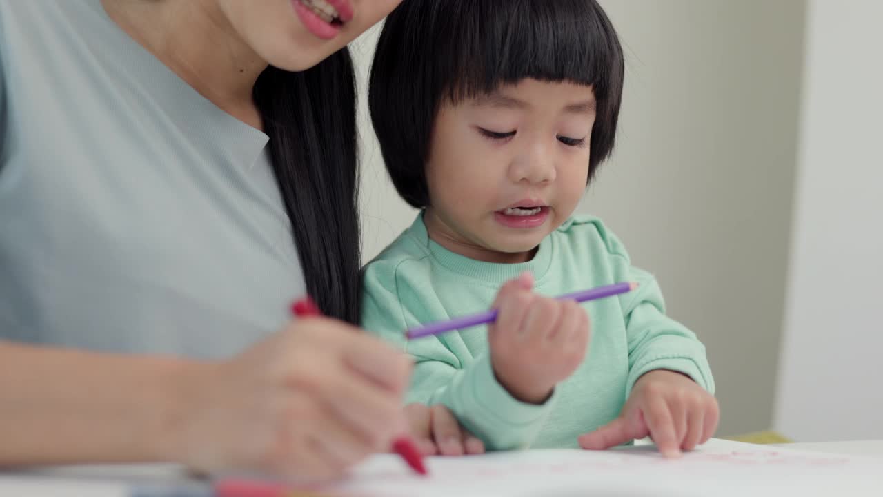 妈妈教儿子如何用蜡笔在书上画画或做作业。快乐的亚洲男孩与他的母亲在客厅里用蜡笔和彩色铅笔画画。家庭的概念。视频素材