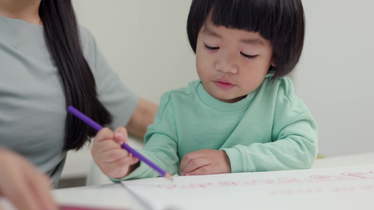 妈妈教儿子如何用蜡笔在书上画画或做作业。快乐的亚洲男孩与他的母亲在客厅里用蜡笔和彩色铅笔画画。家庭的概念。视频素材