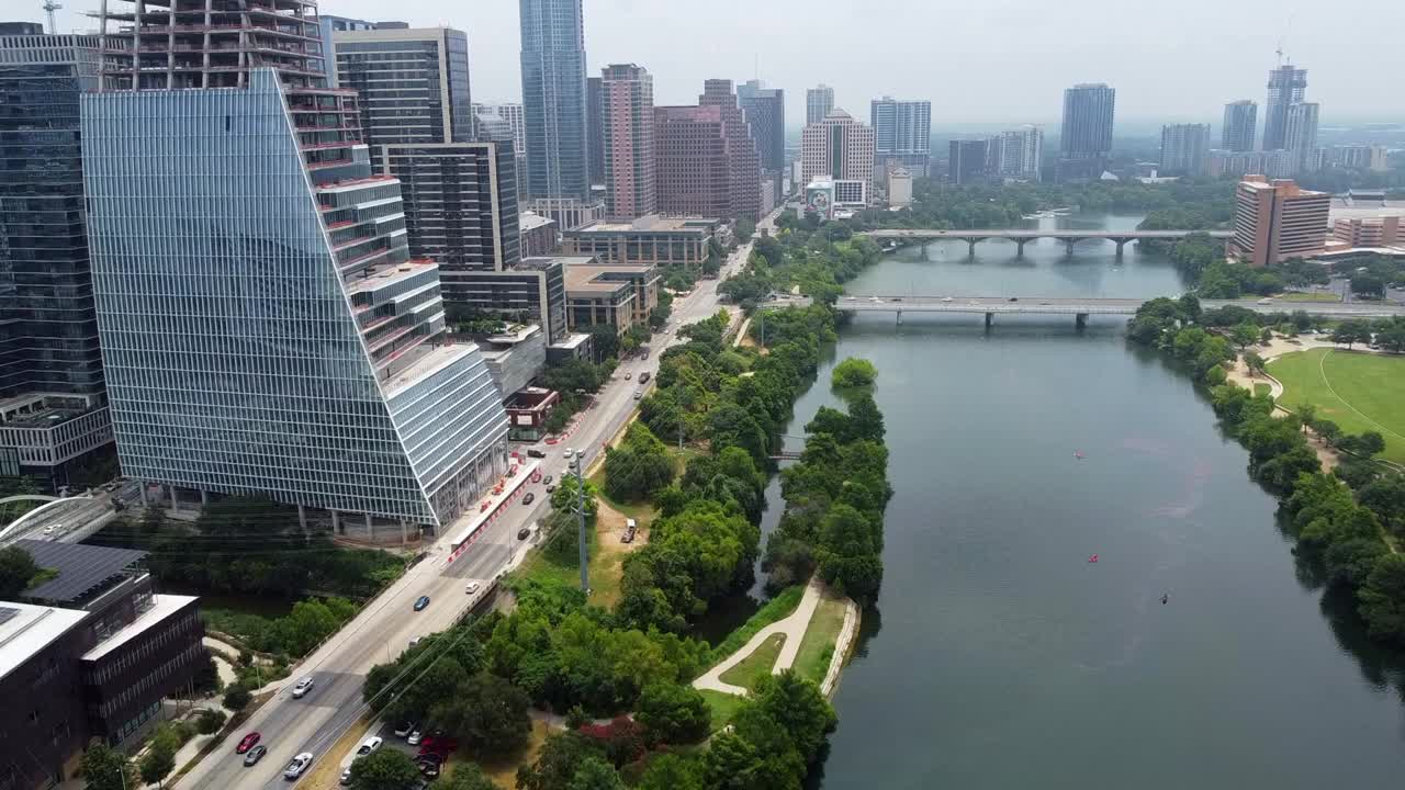 航拍车辆沿着现代建筑和河流的道路，无人机在阳光明媚的日子飞行在城市上空-奥斯汀，德克萨斯州视频素材