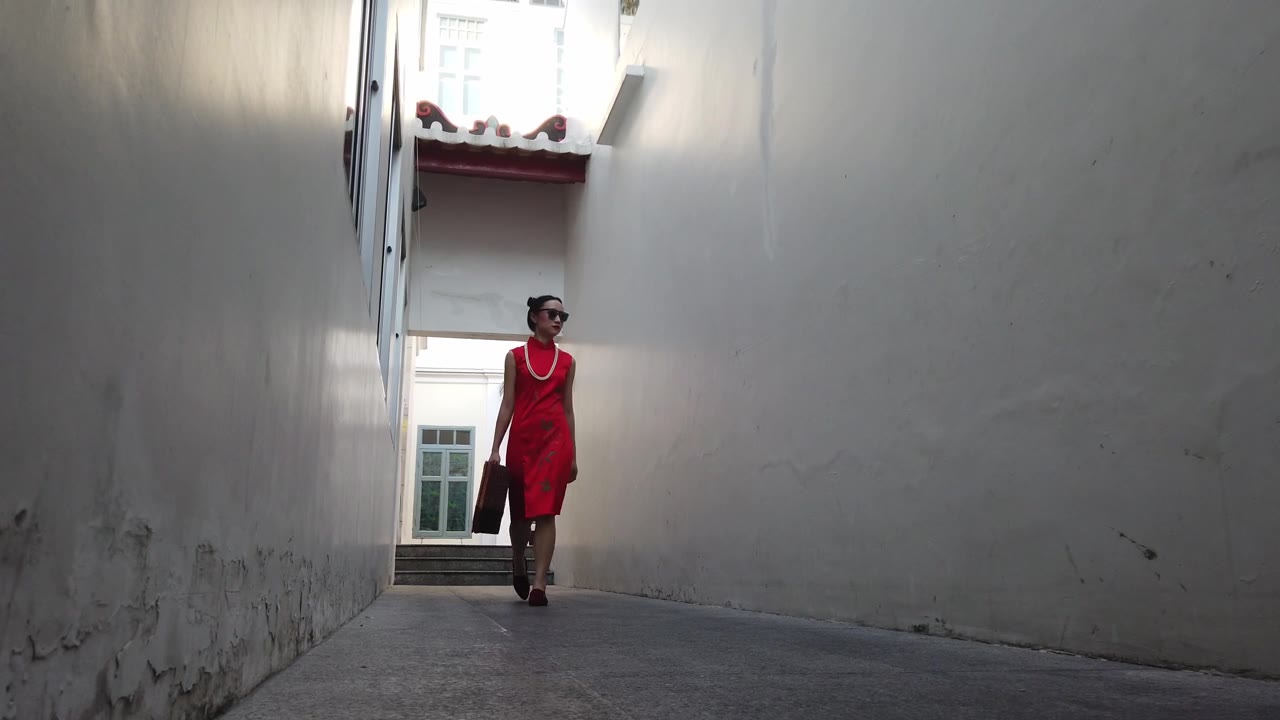 中国年轻女性时装模特在旅行者主题复古中国旗袍走过一个小建筑小巷。视频素材画面1