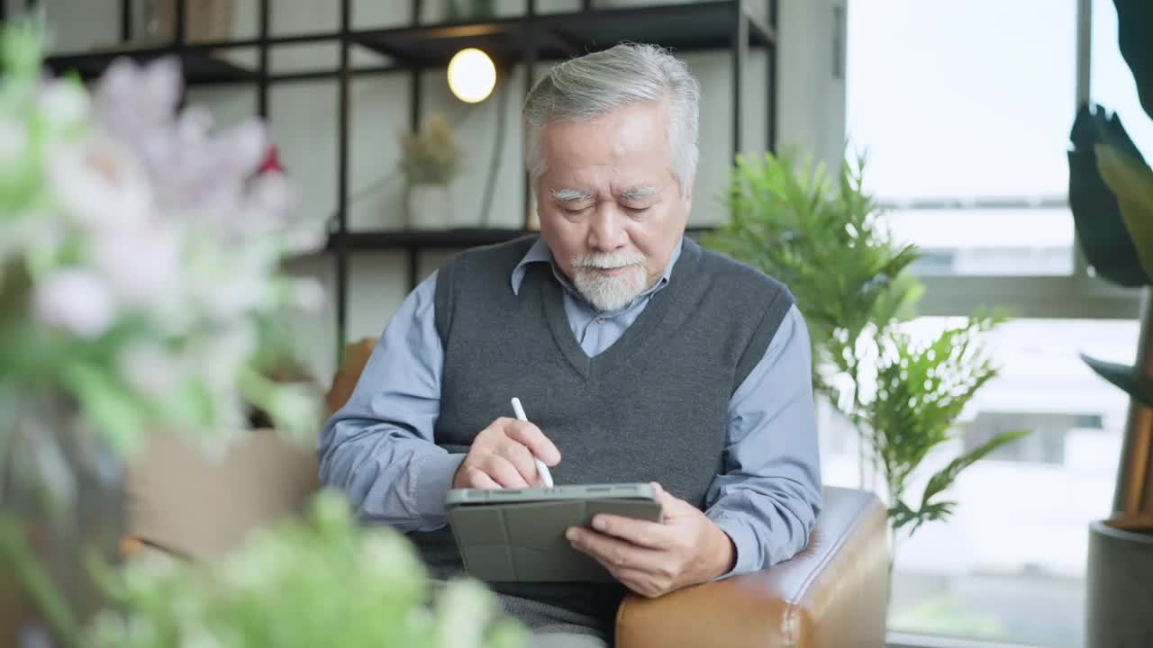 亚洲老人退休老人手使用平板电脑冲浪社交媒体浏览朋友在线社交交流距离连接，幸福亚洲老人呆在家里使用平板电脑在家里视频素材