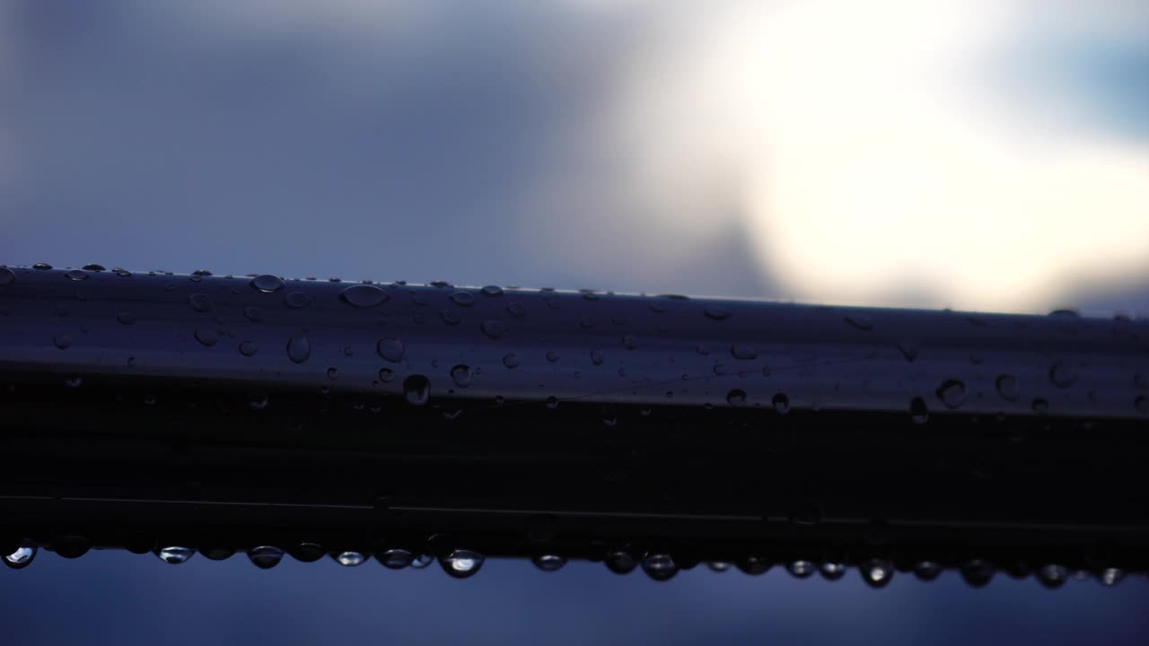 雨滴落在不锈钢扶手上，映衬着模糊的大海背景。特写镜头。雨露中的水滴聚集在闪亮的镀铬钢杆扶手上视频素材