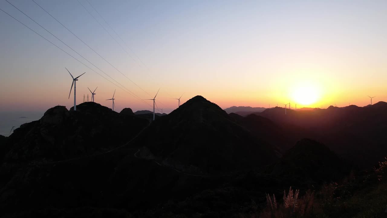 在日落时，一排风力涡轮机在山顶上视频素材