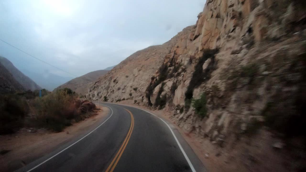 在路上的巴士旅行的POV，雨水淋湿了挡风玻璃，周围是山和蓝天视频素材