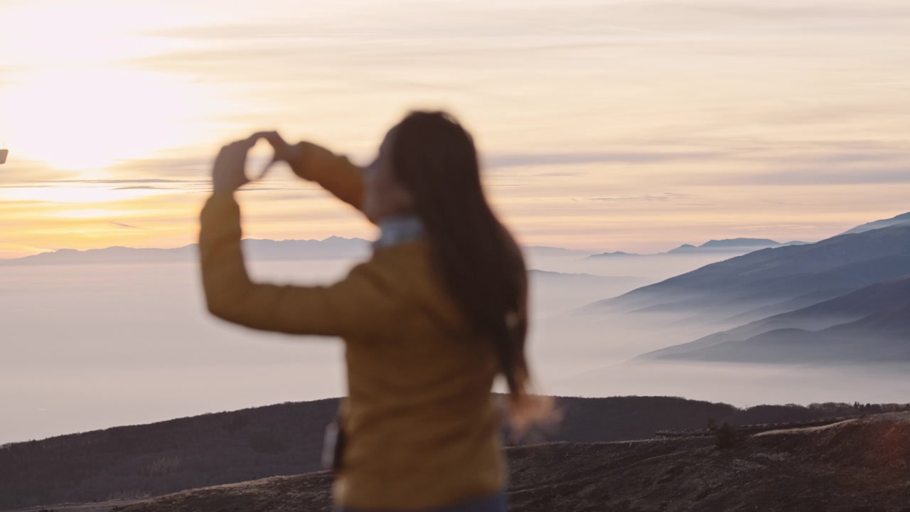 在山峰上的女人在云上享受日落。崇高的观点。视频素材画面2
